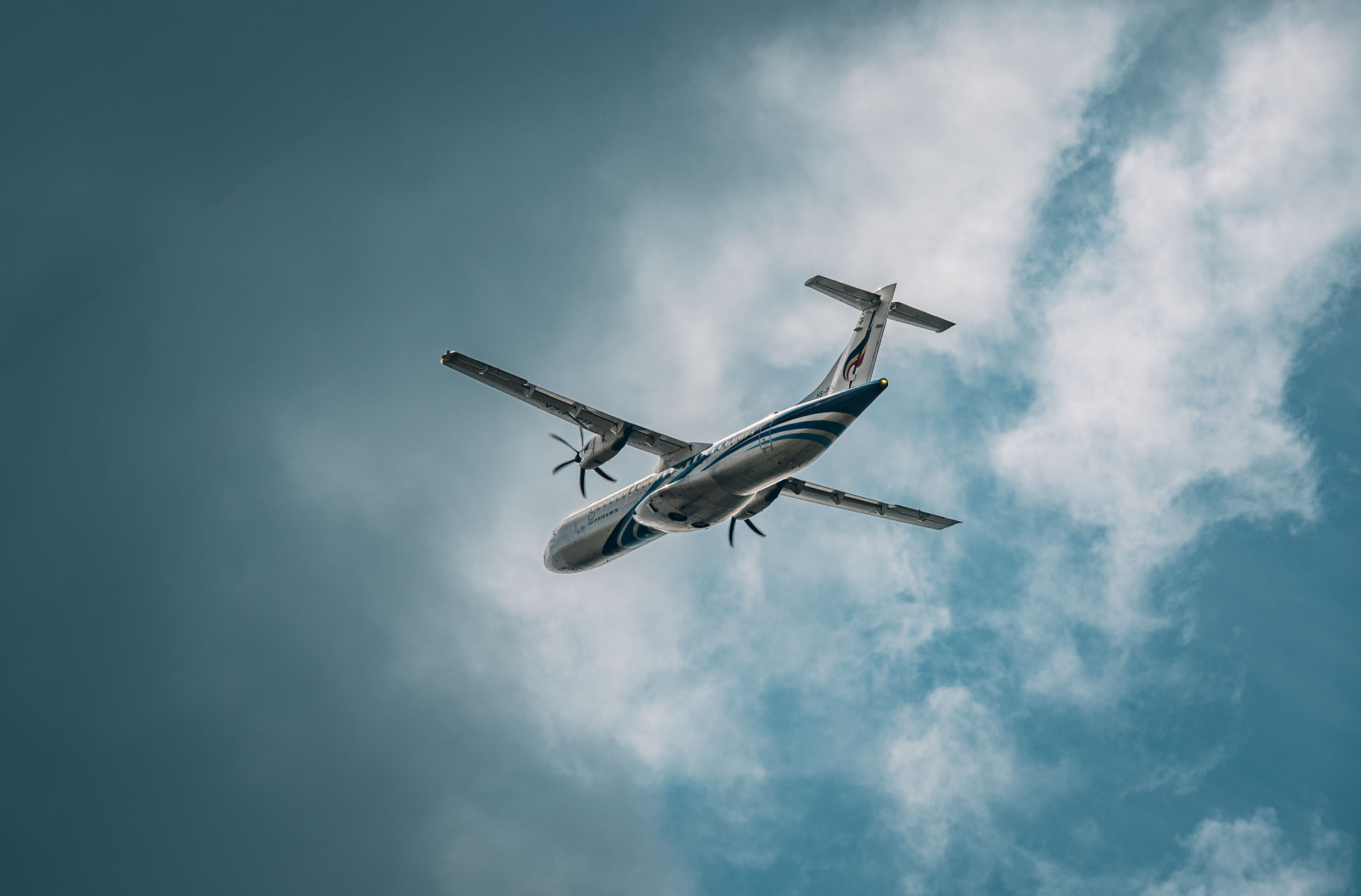 Twin-turboprop airliner seen from below against a cloudy sky