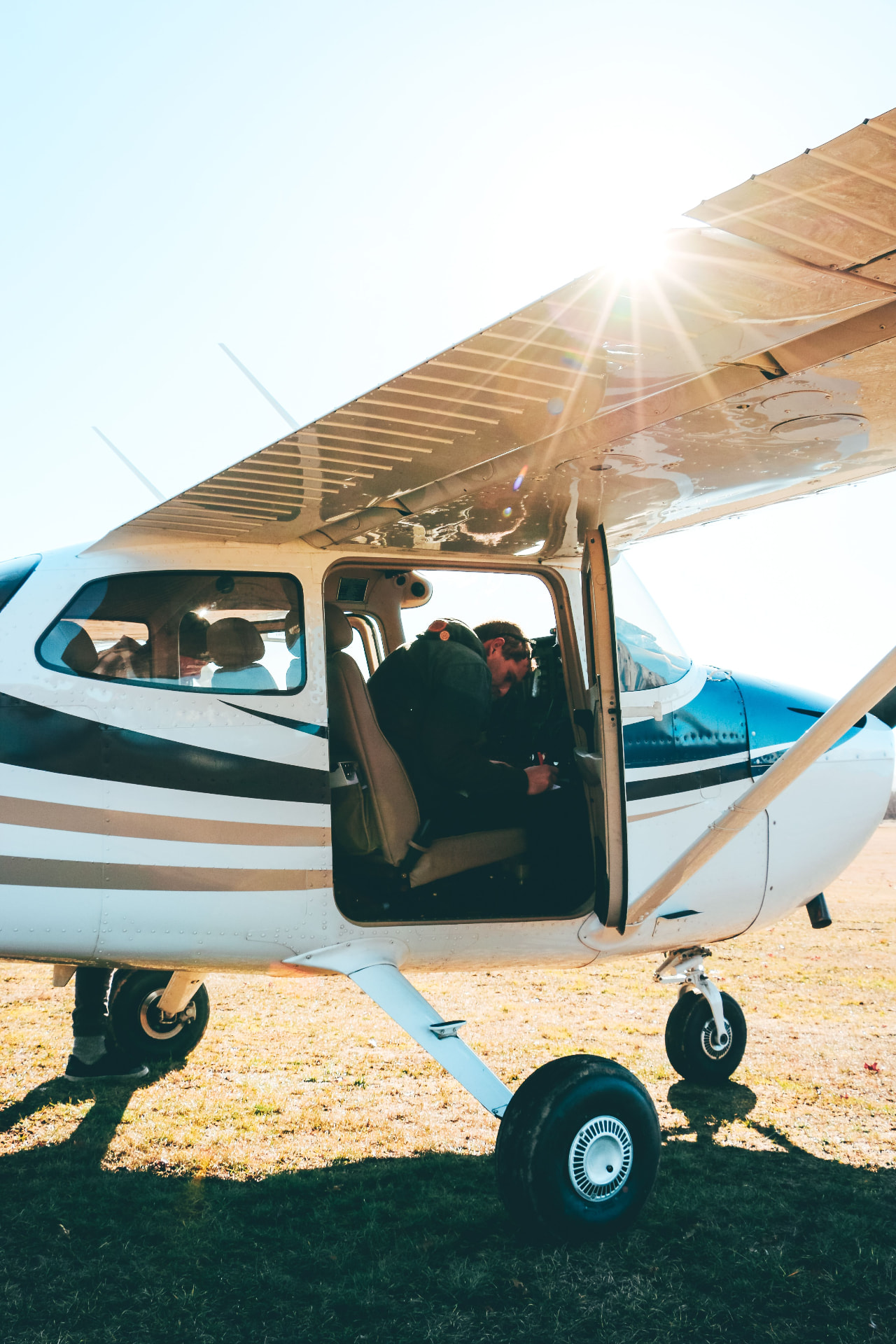 Pilots seated in a light aircraft with the cabin door open in the sun